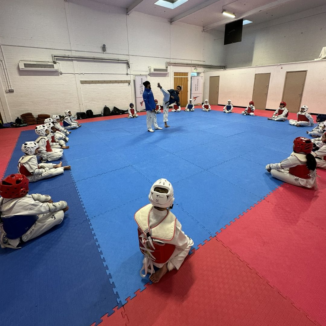 Coach demonstrating a high kick to a seated circle of students